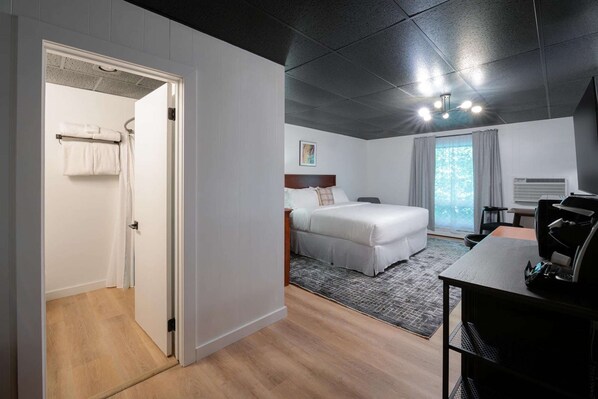A modern hotel room with a bed, a desk, and a shower area. - Trailhead by Weekender (Tupper Lake)