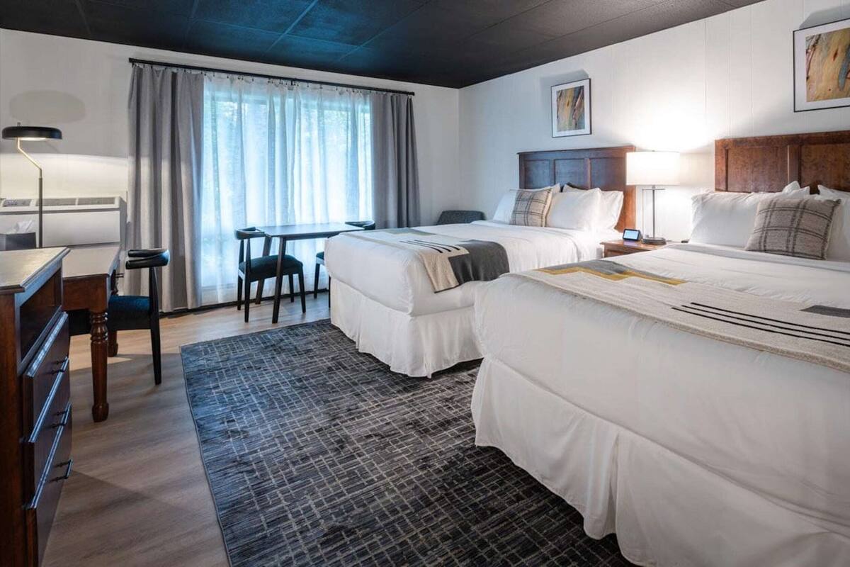 A hotel room with two beds, a desk, a chair, a lamp, and a window with curtains.