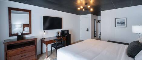 A hotel room with a large bed, a desk with a chair, a flat-screen TV, a dresser, and a ceiling light fixture.