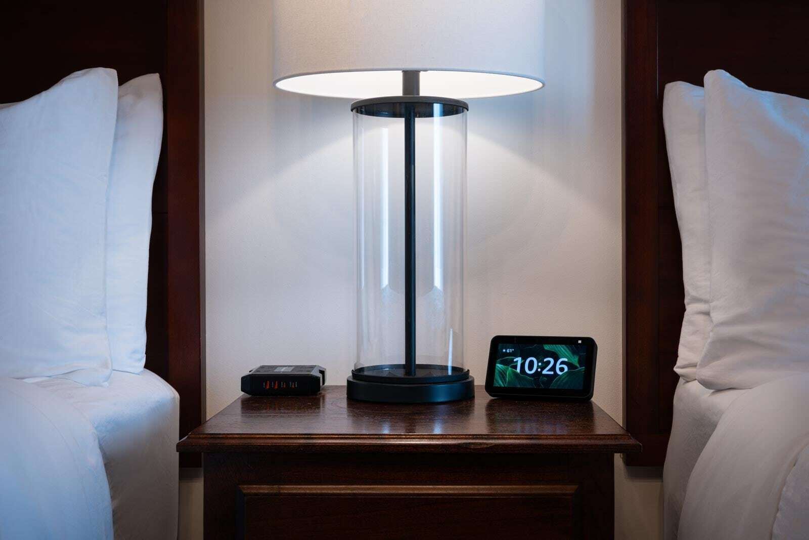 A bedside table with a lamp, a clock displaying 10:26, and a remote control.