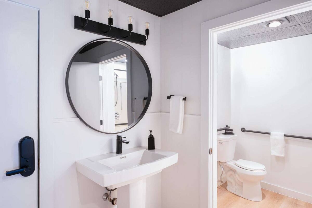 A modern bathroom with a round mirror, a white sink, and a toilet.