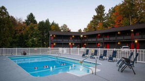 A swimming pool with lounge chairs, a fenced deck, and a building with multiple balconies. - Trailhead by Weekender (Tupper Lake)