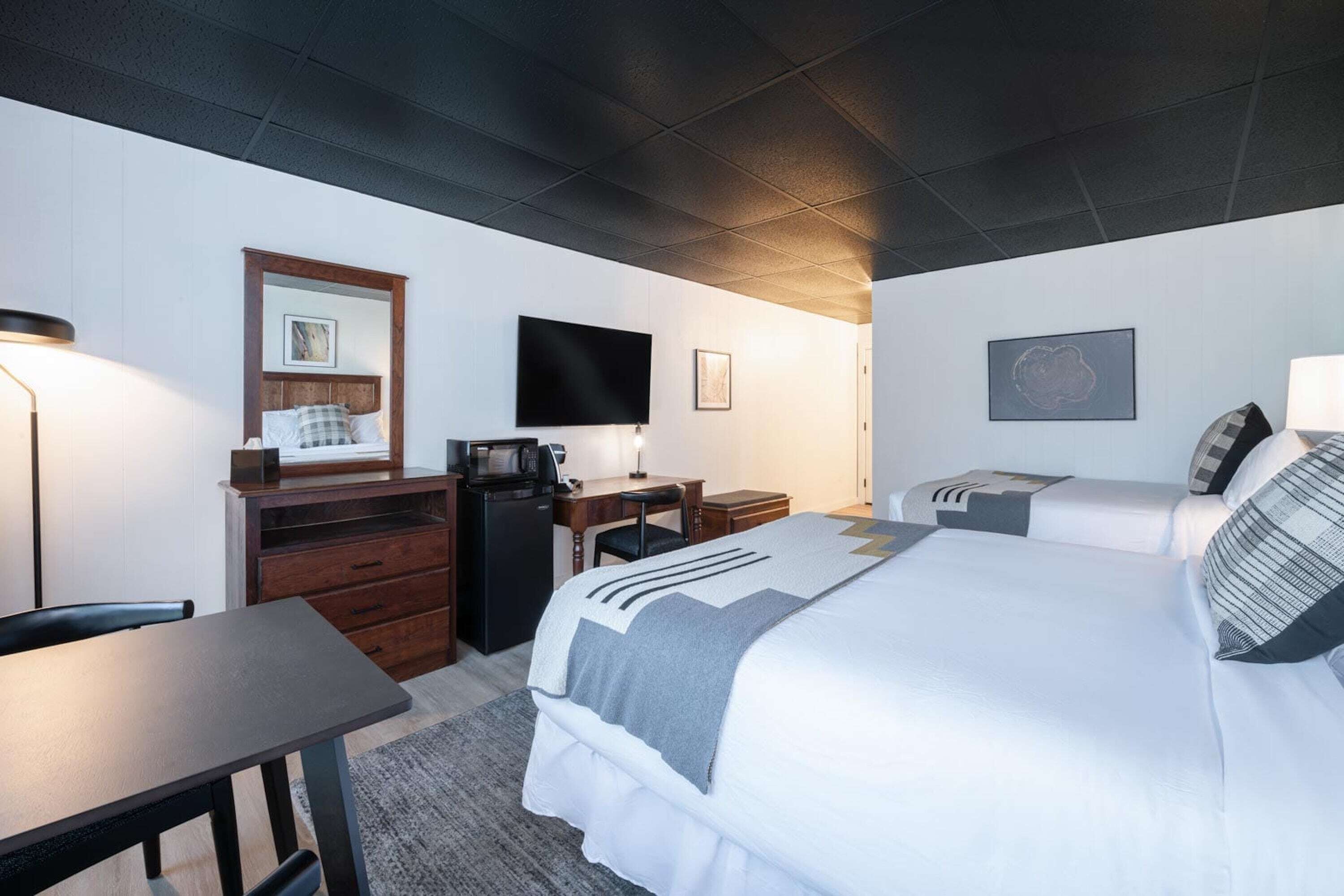 Habitaci ón de hotel con cama, escritorio, silla, televisor y pequeña kitchenette.