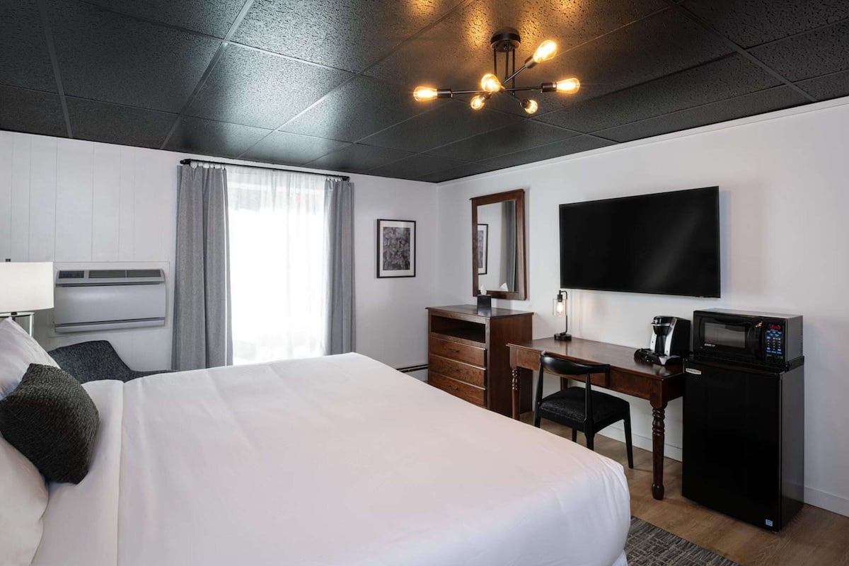 A hotel room with a large bed, a desk with a chair, a flat-screen TV, a microwave, and a window with curtains.