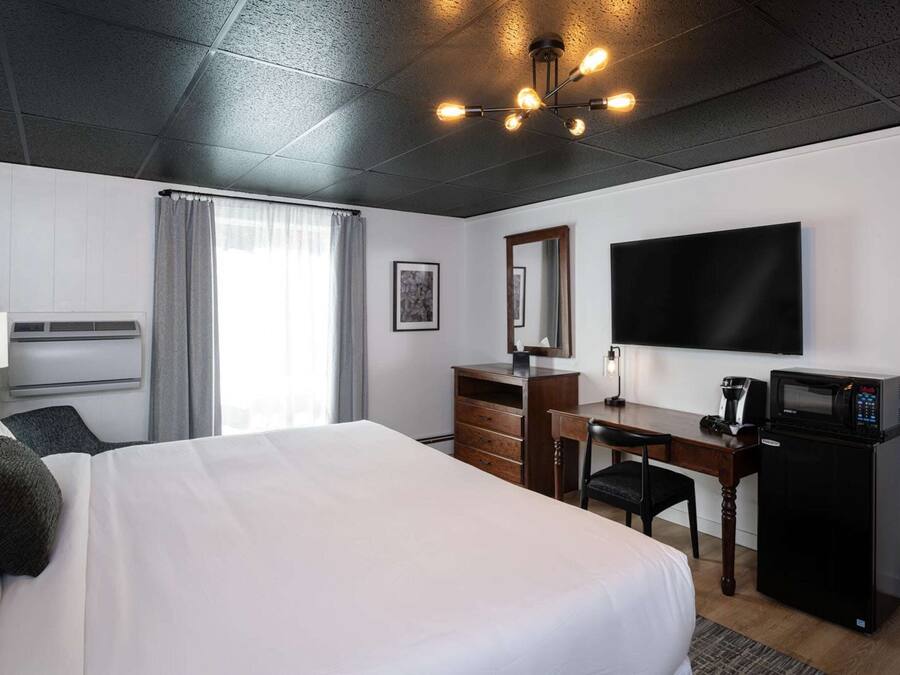 A hotel room with a large bed, a desk with a chair, a flat-screen TV, a microwave, and a window with curtains.