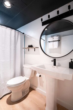 Un baño moderno con inodoro blanco, un espejo redondo y lavamanos blanco.