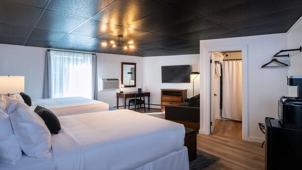 A hotel room with two beds, a desk, a TV, and a wardrobe. - Trailhead by Weekender (Tupper Lake)