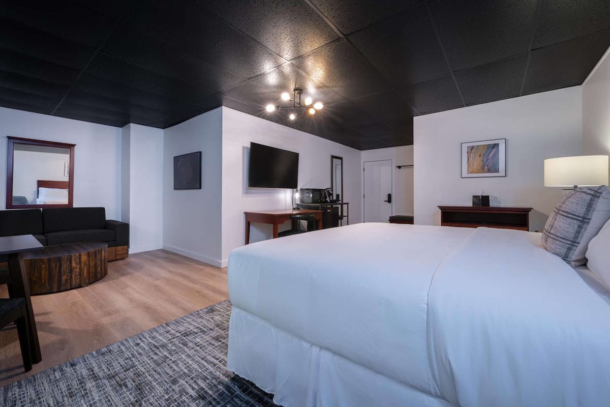 A modern hotel room with a large bed, a flat-screen TV, a desk, and a sofa.