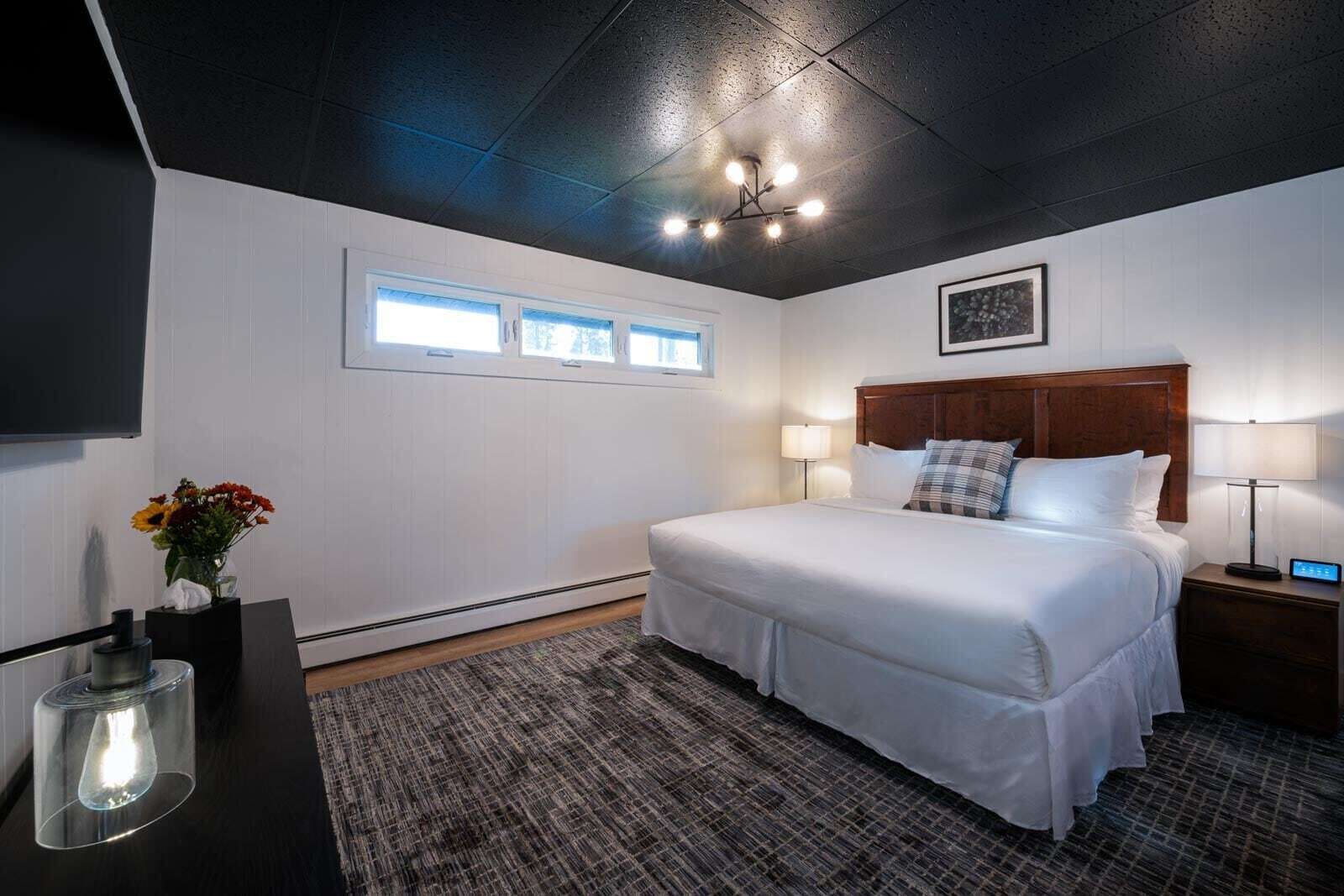 Une chambre d’hôtel avec un grand lit, des lampes de chevet, une table de chevet, un bureau avec une lampe et une fenêtre avec des stores.