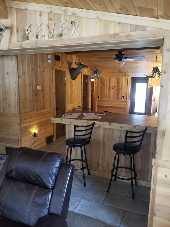 Un interior de madera con una zona de bar, dos taburetes negros, un sofá de cuero y adornos de asta.