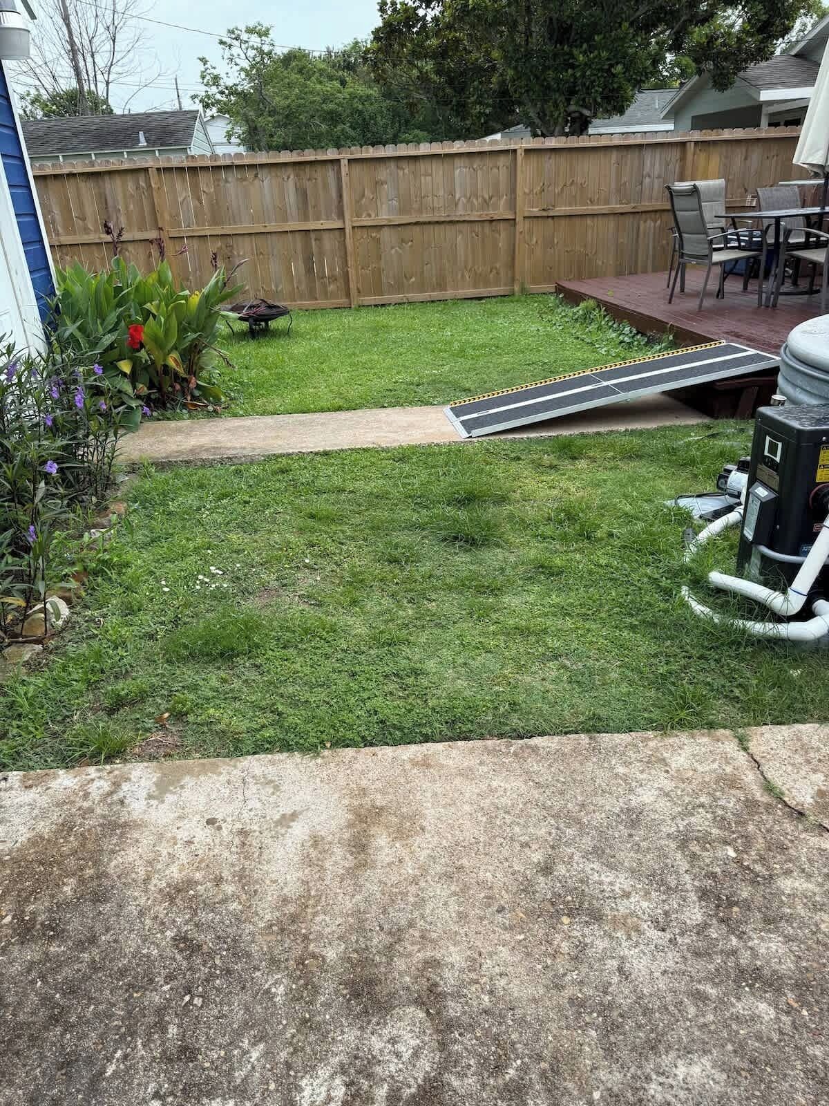 Un jardin avec une clôture en bois, une terrasse en béton et une pelouse.