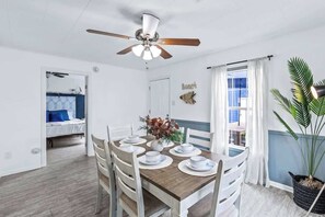 A dining area with a wooden table set for six, a ceiling fan, a potted plant, and a view of the outside.