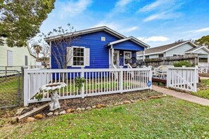 A single-story house with a blue exterior, a white picket fence, and a small garden area with a birdbath.