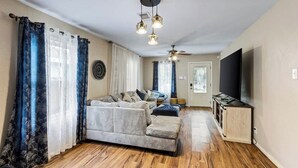 A living room with a sofa, curtains, a ceiling fan, and a TV.