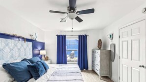 A bedroom with a bed, a ceiling fan, a dresser, a wardrobe, and a window with curtains.