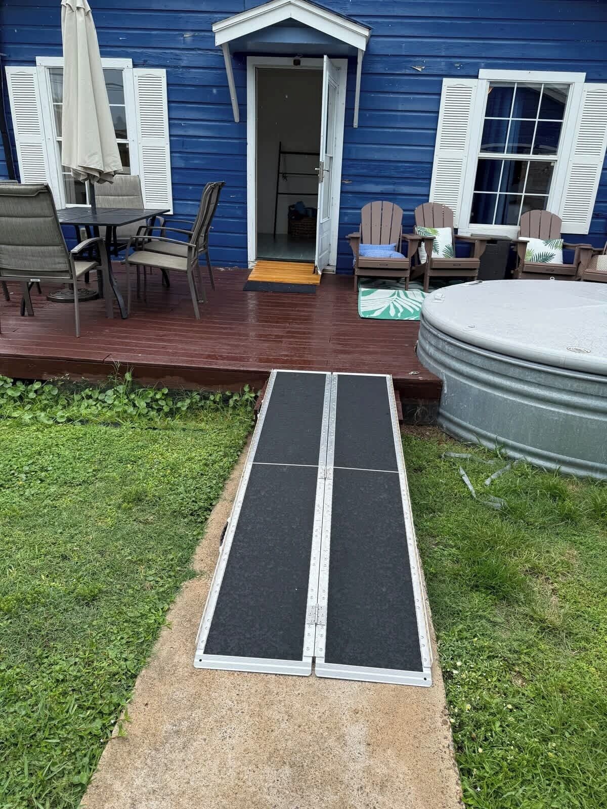A blue house with a covered patio, a hot tub, and a ramp leading to the entrance.