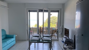 Ein Wohnzimmer mit Esstisch, Stühlen, einer Couch, einem Fernseher und einem Kühlschrank.