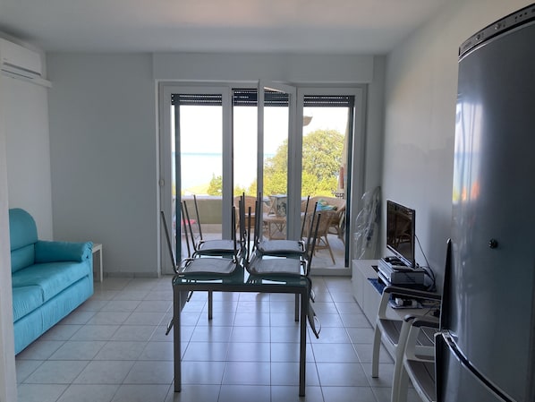 Un salon comprenant une table à manger, des chaises, un canapé, un téléviseur et un réfrigérateur.
