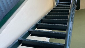 Eine Metalltreppe mit Handlauf, die zu einem Fenster mit Jalousien führt.