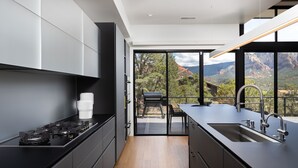 A modern kitchen with black cabinetry, a stainless steel stove, and a large window overlooking a mountainous landscape.