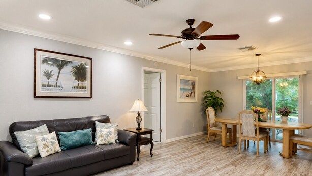 A living room with a dark leather sofa, a dining table with chairs, a ceiling fan, and a window with a view of greenery. - Cozy home in quiet neighborhood!! LLC.              2 Kings  bed and 1 Queen  (Spring Hill)