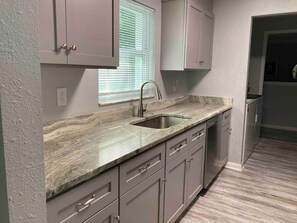A kitchen with a marble countertop, stainless steel sink, and grey cabinets. - Cozy home in quiet neighborhood.2king beds (Spring Hill)
