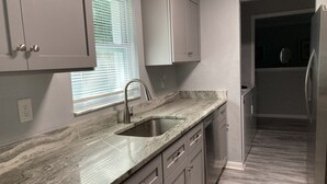 A kitchen with a granite countertop, stainless steel sink, and a built-in dishwasher. - Cozy home in quiet neighborhood!! LLC.              2 Kings  bed and 1 Queen  (Spring Hill)