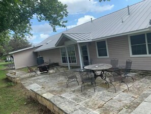 A house with a covered patio area featuring a stone patio, metal outdoor furniture, and a large window. - Quiet, Comfy Wine Trail Home (Johnson City)