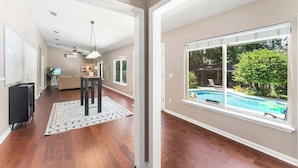 Una habitación amplia con pisos de madera, un ventanal con vista a una piscina y un ventilador de techo.