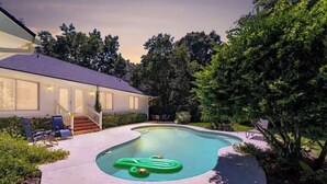 Una piscina con un tobogán inflable verde, un porche cubierto con sillas y una casa con terraza techada.
