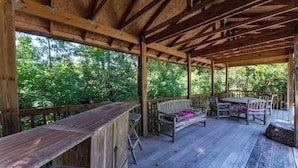 Una terraza exterior de madera con un banco y una mesa de madera, rodeada de exuberante vegetación.