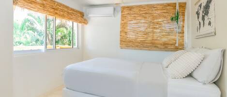 A bedroom with a bed, a window with a view of greenery, an air conditioning unit, and a world map on the wall.
