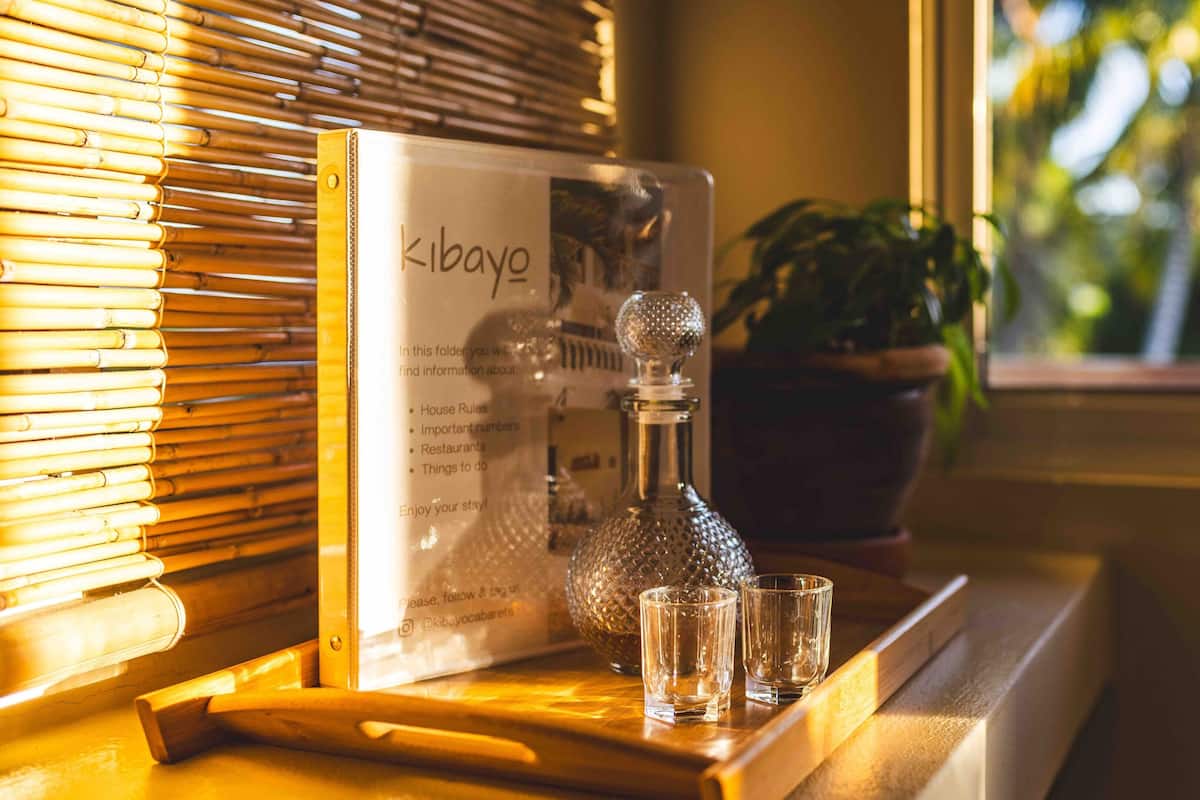 A wooden table with a glass decanter, two glasses, and a booklet titled 'Kibayo'.