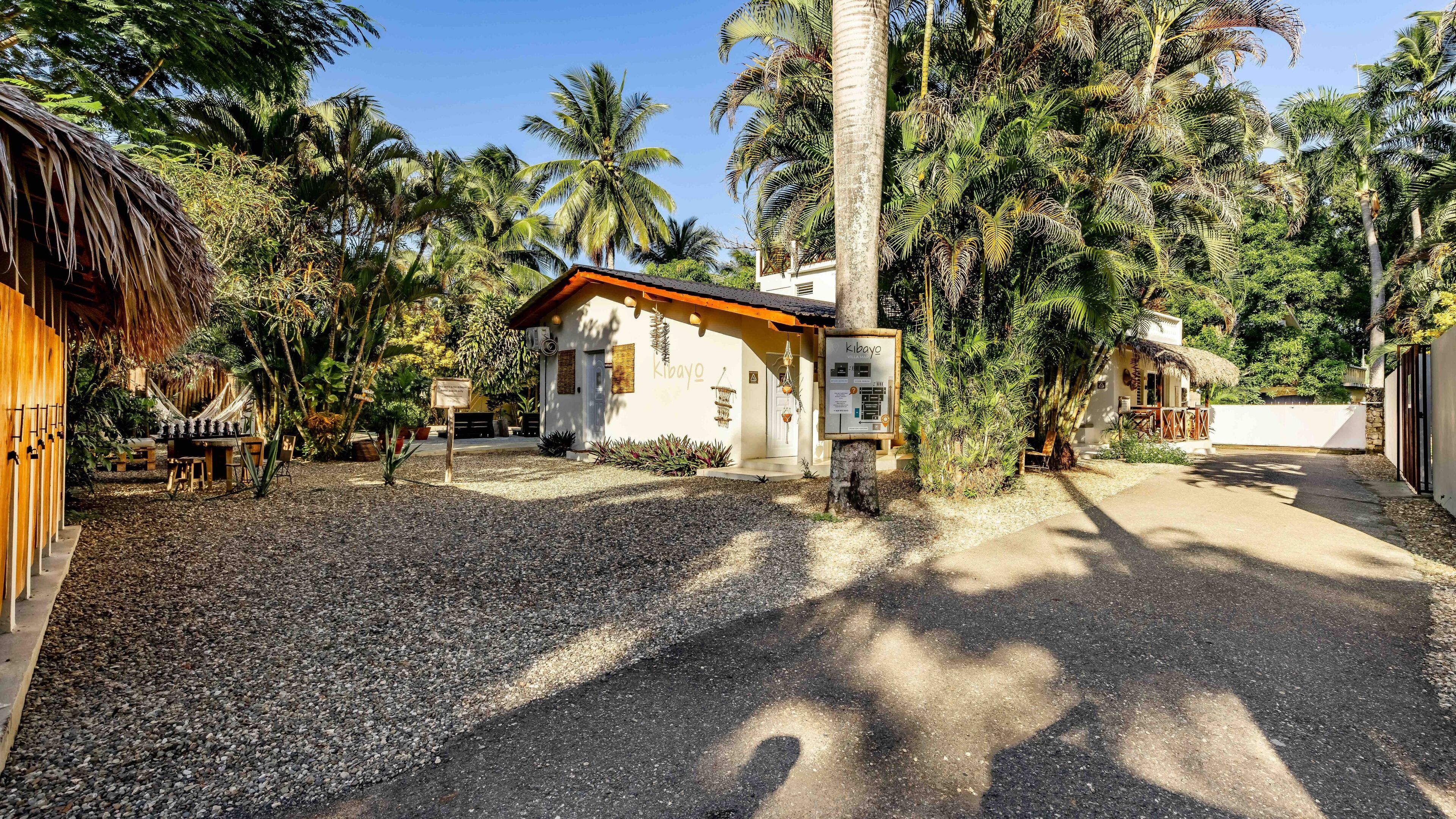 A resort with a thatched-roof building, palm trees, and a gravel driveway.