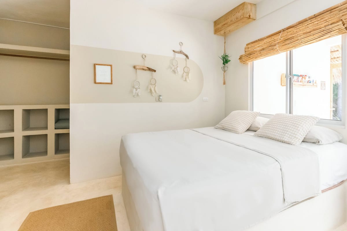 A bedroom with a large bed, a wall-mounted shelf, and a window with a view.
