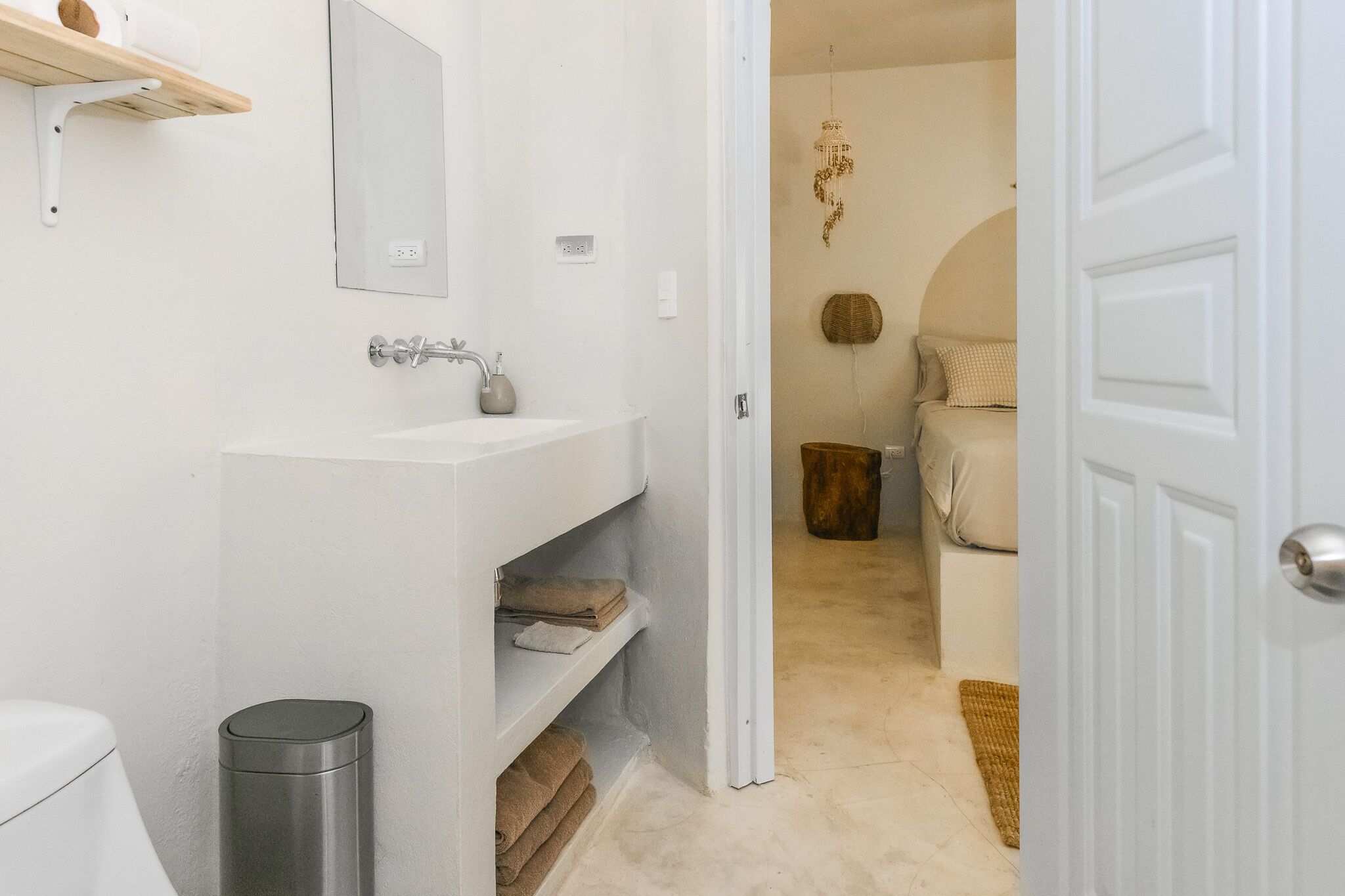A bathroom with a white sink, mirror, and shelves with towels.