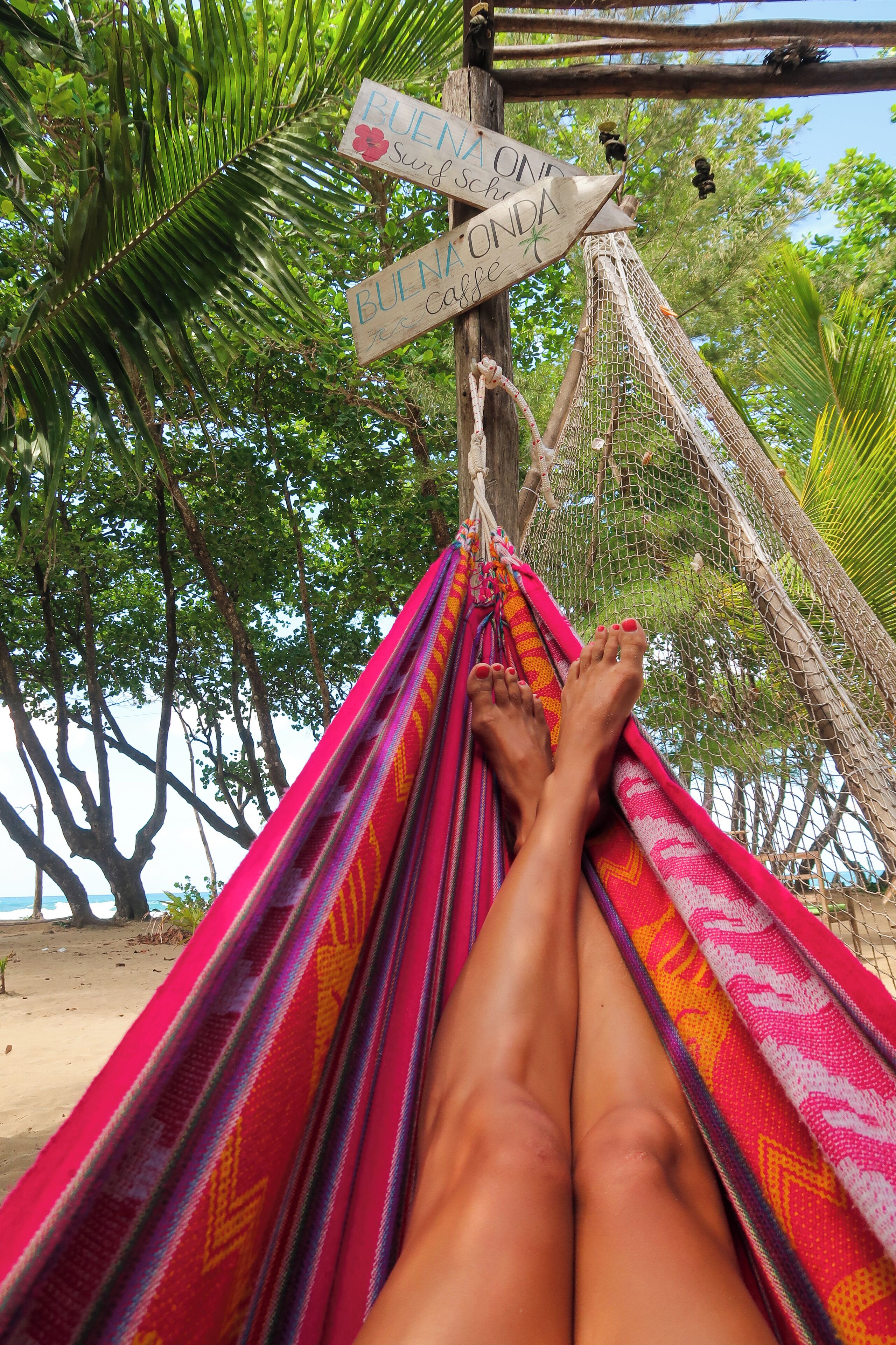 A hammock tied to a tree with a sign reading "BUENA ONDA".
