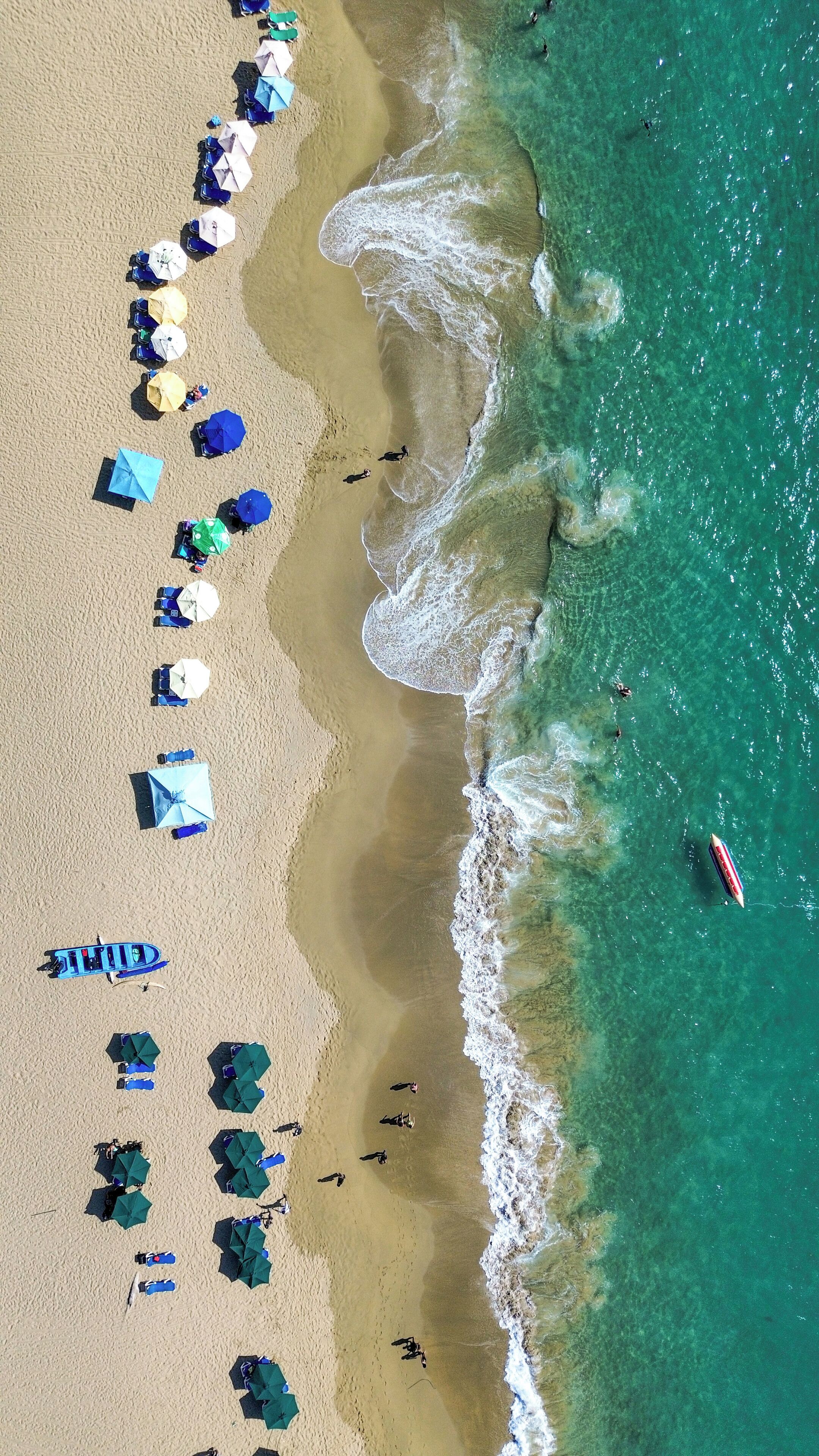 An aerial view of a beach with rows of umbrellas and beachgoers.