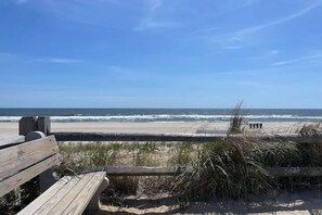 A beach with a wooden bench, a sandy path, and the ocean in the background.