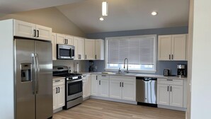 Una cocina moderna con armarios blancos, electrodomésticos de acero inoxidable, horno empotrado y una ventana con persianas.