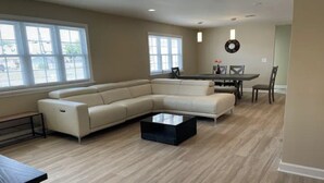 Un salón amplio con un sofá seccional en forma de L, una mesa de centro y una zona de comedor con una mesa y sillas.