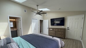 Un dormitorio con cama, ventilador de techo, televisión montada en la pared y cómoda.