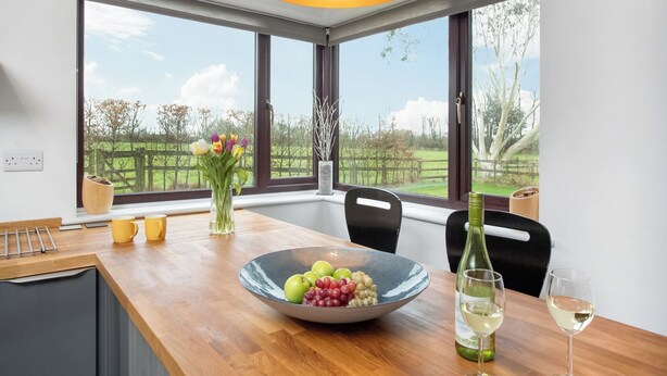 A dining area with a wooden table, a bowl of fruit, two wine glasses, and a vase with flowers. - 4 bedroom accommodation in Blackdown Hills, near Culmstock (Blackdown Hills, near Culmstock)
