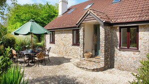 A stone house with a tiled roof, a patio with a table and chairs, and a green umbrella. - 4 bedroom accommodation in Blackdown Hills, near Culmstock (Blackdown Hills, near Culmstock)
