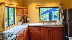 Une cuisine avec des meubles en bois, une cuisinière à gaz, un évier et une fenêtre donnant sur un paysage verdoyant.