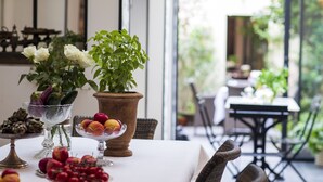 A dining table with a white tablecloth, surrounded by wicker chairs. There are various fruits and flowers on the table. - LA Maison Bordeaux: Celebrating Lifes Pleasures, the French Way (Bordeaux)