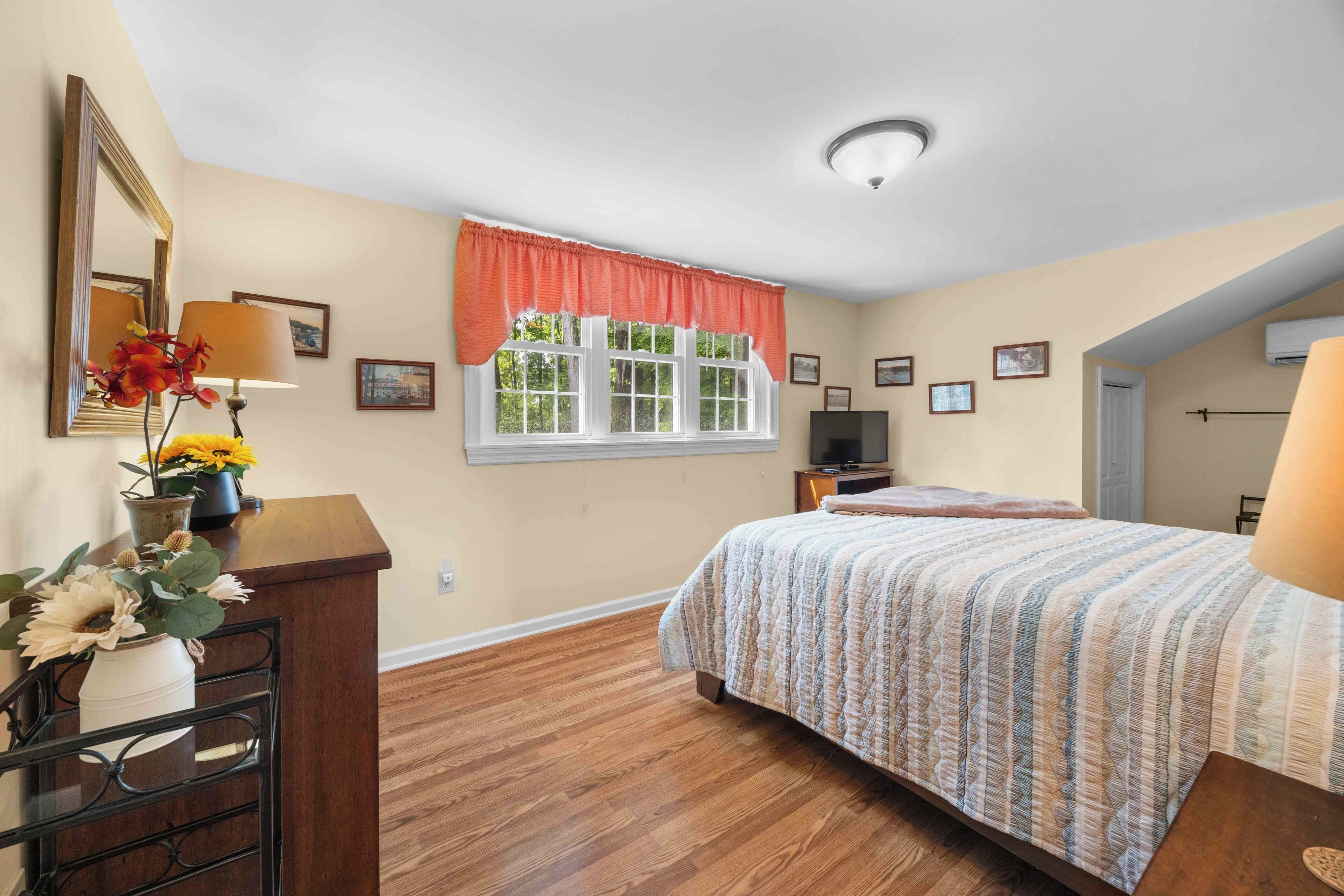 A bedroom with a bed, a dresser, a TV, and a window with a view of trees.