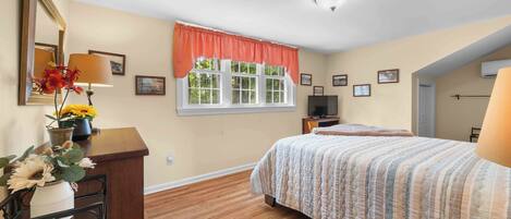 Un dormitorio con cama, cómoda, televisor y ventana con vista a árboles.