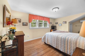 Een slaapkamer met een bed, een dressoir, een televisie en een raam met uitzicht op bomen.