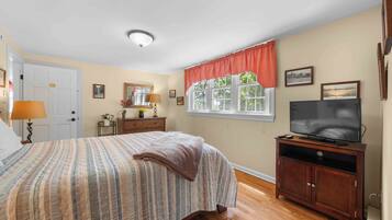 Une chambre à coucher avec un lit, une commode, un téléviseur et une fenêtre avec des rideaux.